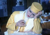 A woman in yellow suit drinks an alcoholic beverage.